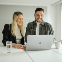 Ein Mann und eine Frau blicken in einen Laptop auf einem Schreibtisch